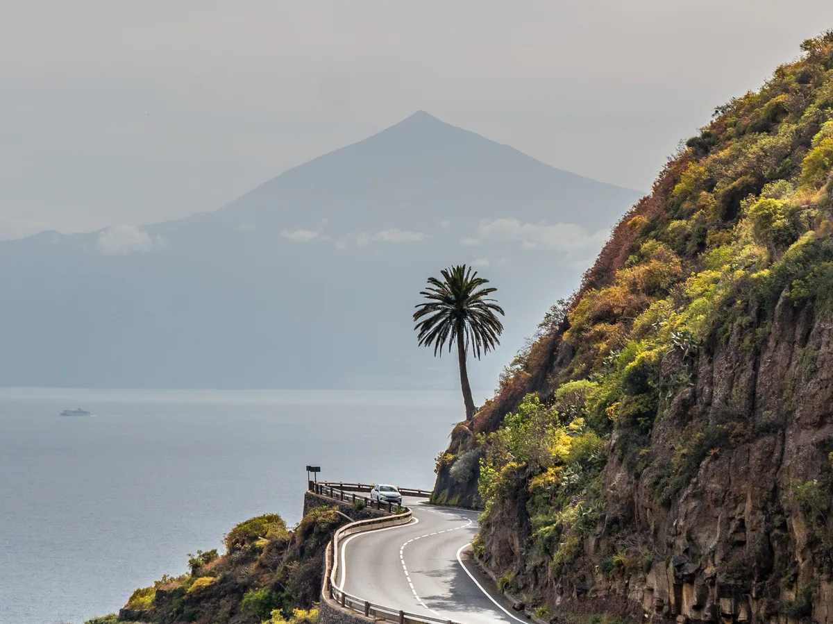Carretera de costa serpenteante en el norte de Tenerife con el Teide al fondo entre brumas